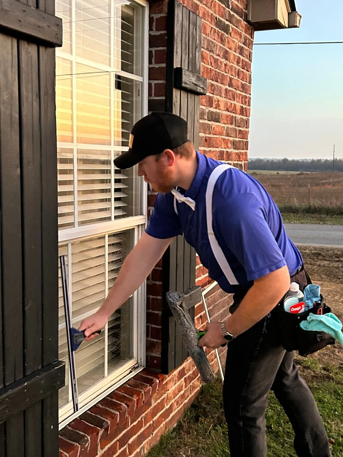 Technician cleaning the outside of a window on a brick house